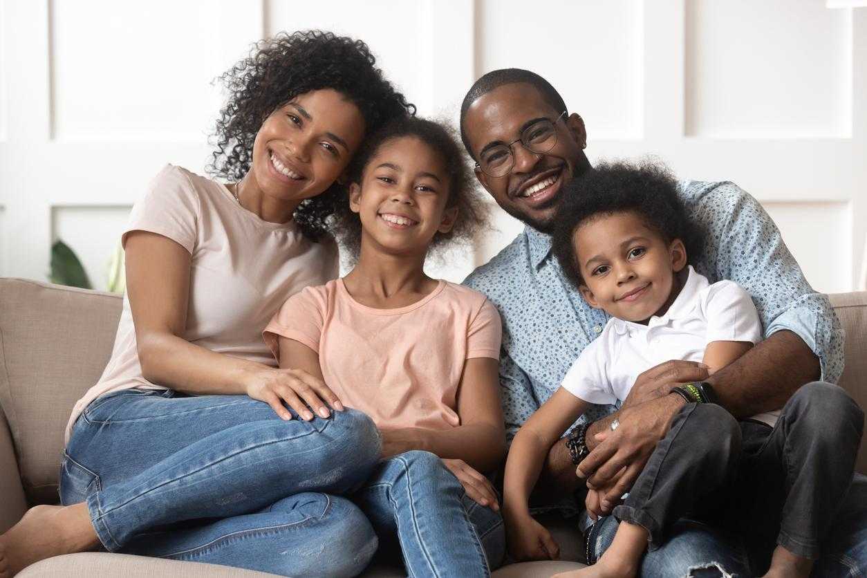 family of four smiling while sitting on couch